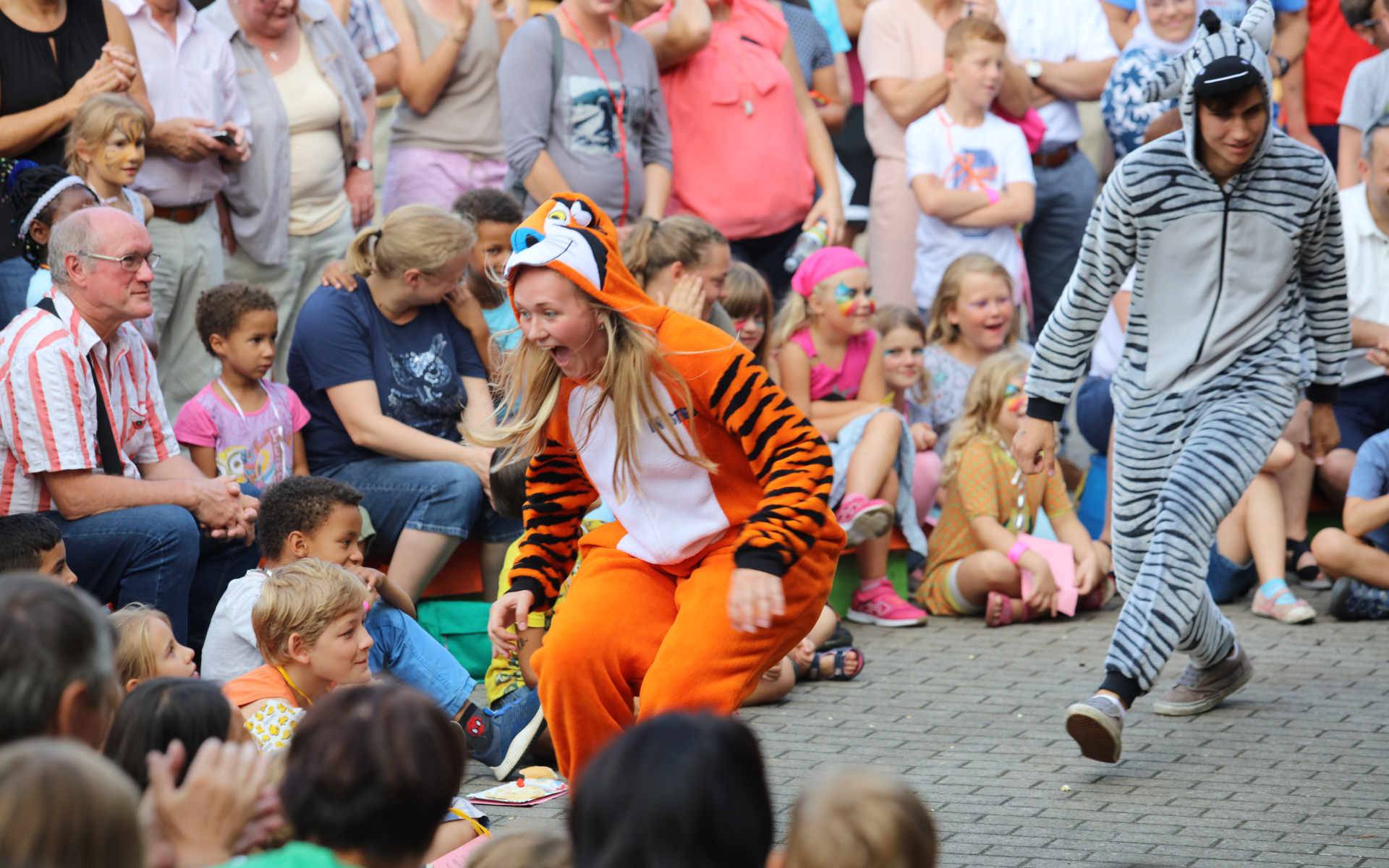Frau springt als Tiger verkleidet in Richtung mehrerer Kinder.